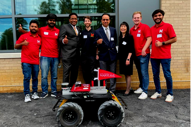 UMD President Darryll J. Pines (third from left), Paul Chrisman Iribe Professor of Computer Science and Electrical and Computer Engineering Dinesh Manocha (fourth from right), and Dr. Barry Mersky and Capital One Endowed Professor of Computer Science Ming Lin (third from right) pose with students in front of a robot equipped with a navigational system developed at UMD. The robot was part of demos that took place during opening ceremonies for the new USMSM SMART Building on October 15.