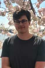 Collin Inglut, smiling with crossed arms in front of a cherry blossom tree