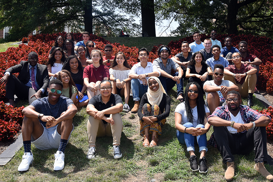 A group of diverse students poses seated on grass for a photo outside.
