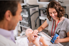 Two clinicians work to demonstrate a device on a doll, modeling a pediatric patient.