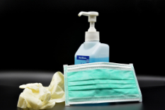 Hand sanitizer, blue medical mask, and yellow rubber medical gloves set against a black background