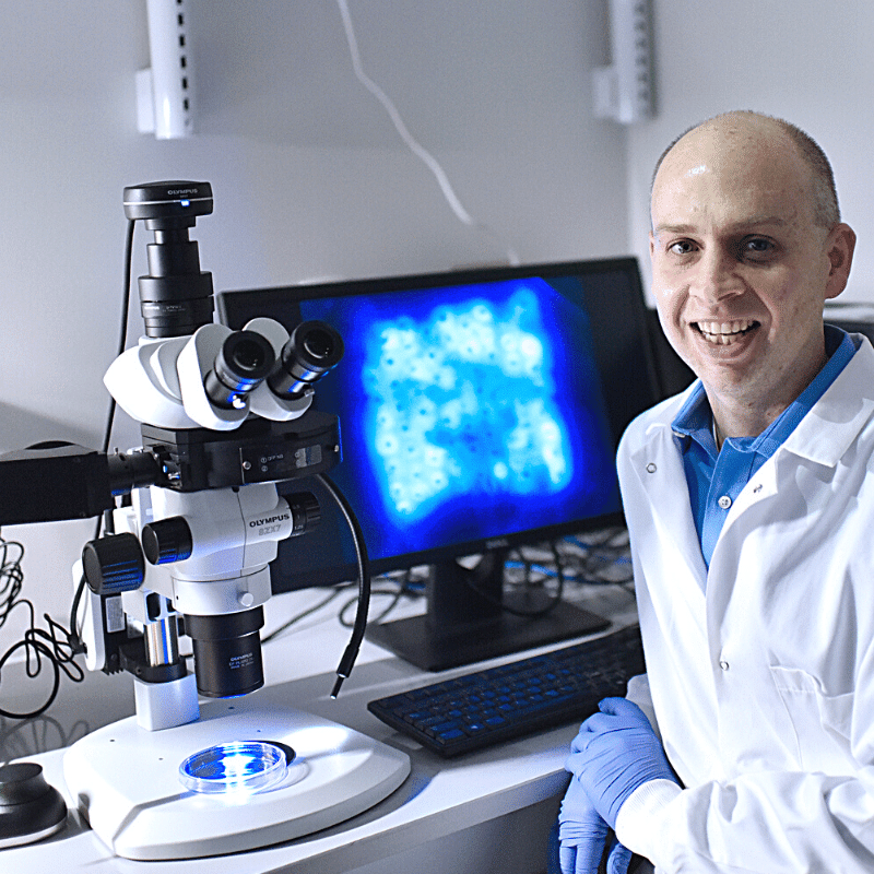 Dr. Chris Jewell sits in front of a microscope in his lab.