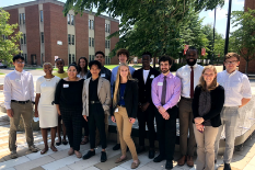 Group of REU students dressed in business attire, smiling outside of A. James Clark Hall