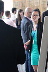 Female student in business attire gesturing towards a research presentation on a poster board