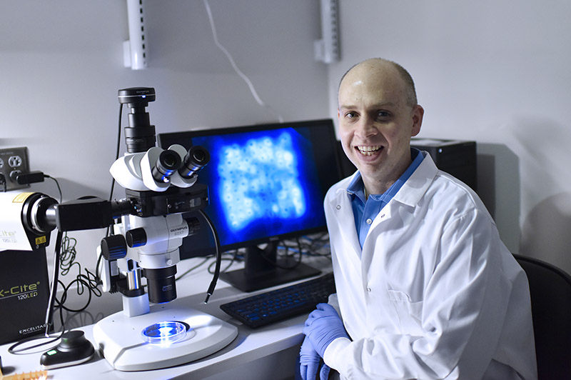 Dr. Christopher Jewell pictured in the lab near a microscope.