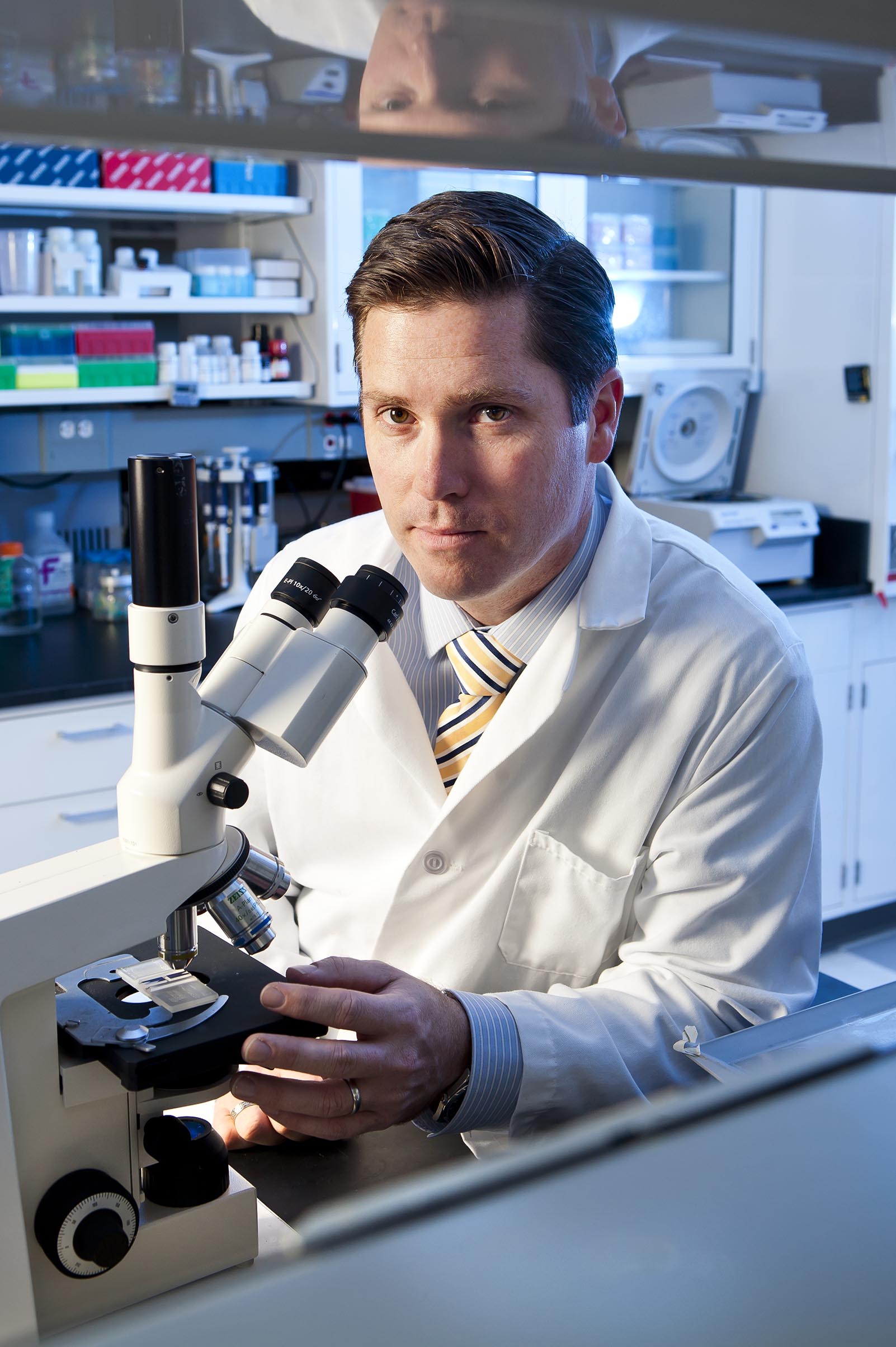 Dr. John Fisher sits behind a microscope in a bioengineering lab