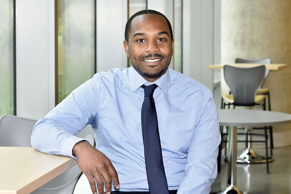 Dr. Gregg Duncan, pictured sitting in front of some tables and chairs and a glass window