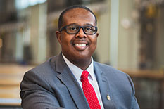 headshot of Dean Graham wearing glasses and a white collared shirt with a red necktie and a gray jacket