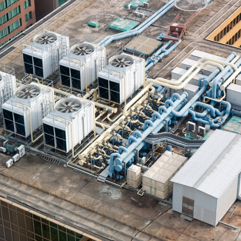 An aerial view of a rooftop HVAC (Heating, Ventilation, and Air Conditioning) system with multiple large white cooling units connected by a network of blue and white pipes on top of a building