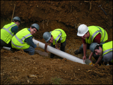 Students from the Anacostia Project team place the outflow pipe from the bioretention facility into the trench before it is filled back over with dirt. (Photo by Kristen Markham)