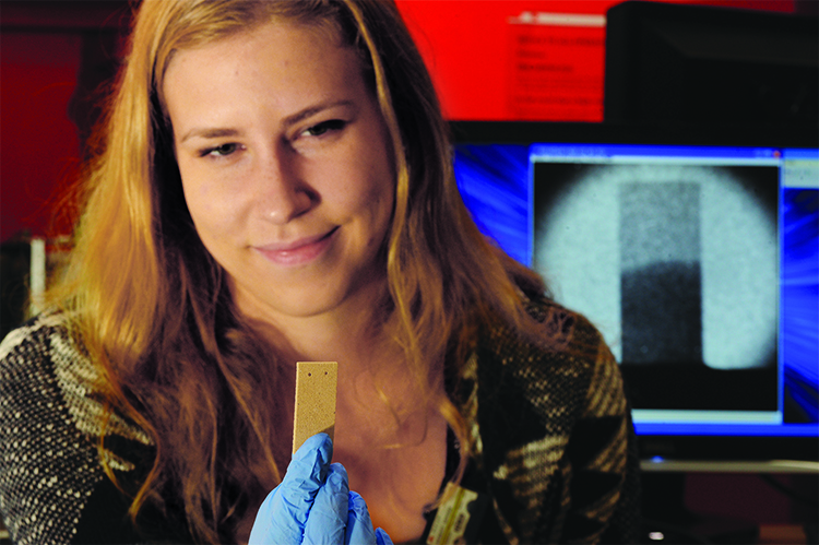 Mimi Hiebert holds a limestone sample; behind her, a screen displays a limestone sample half-soaked with water. Photo: Timothy Koeth